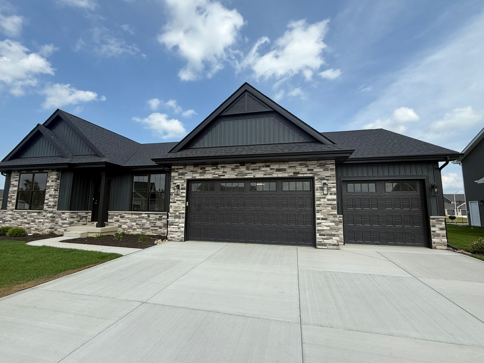 Modern dark-gray brick house with three garages and a wide concrete driveway under a blue sky