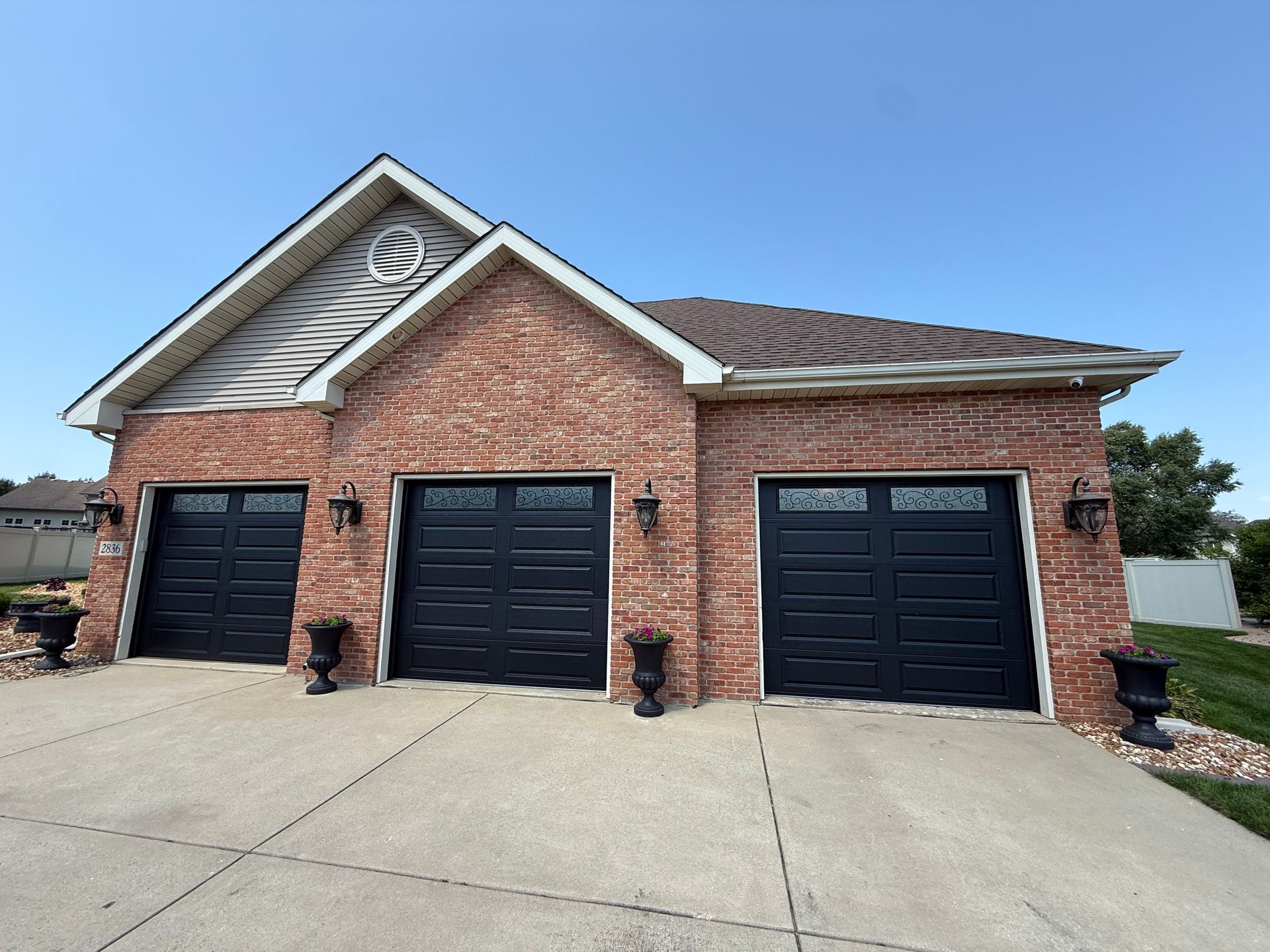 Brick house with three black garage doors and a steep driveway under a clear blue sky