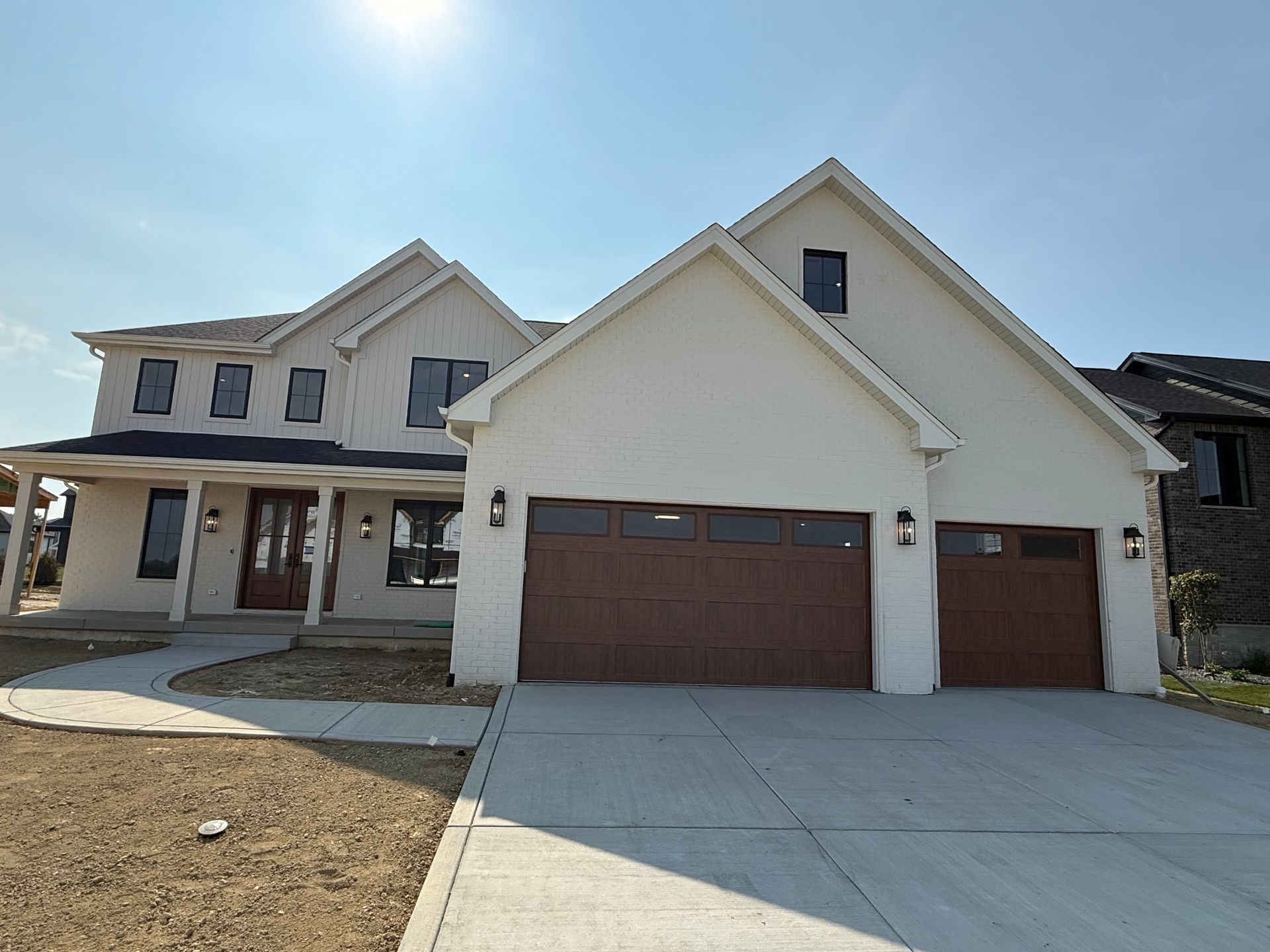 New beige two-story house with brown garage doors and a wide concrete driveway