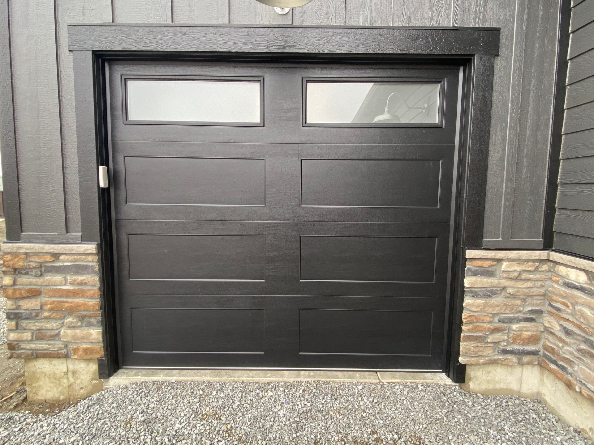 Black double garage door with narrow windows, set in a stone and dark wood exterior.