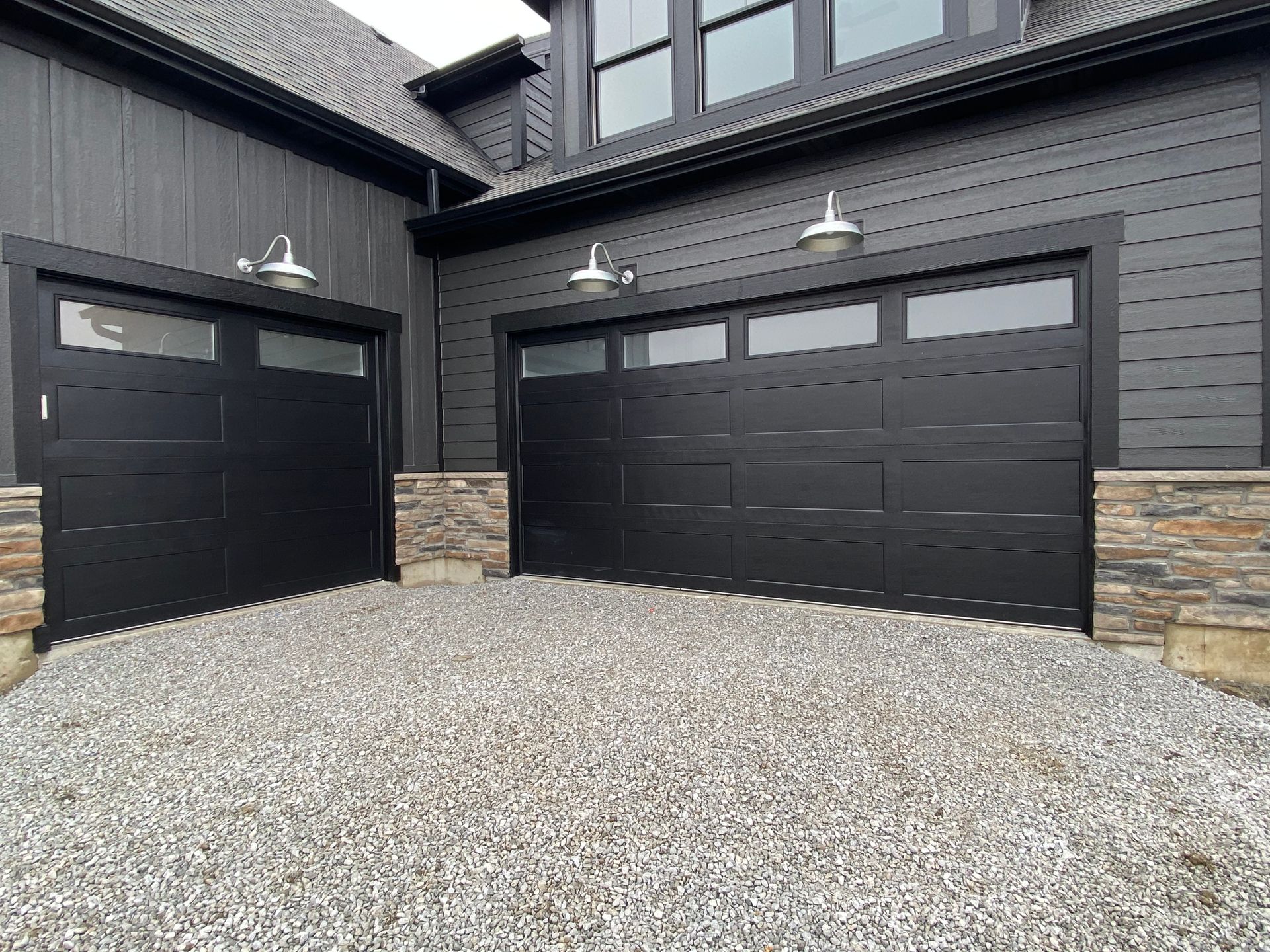 Black house exterior with two garage doors and gravel driveway