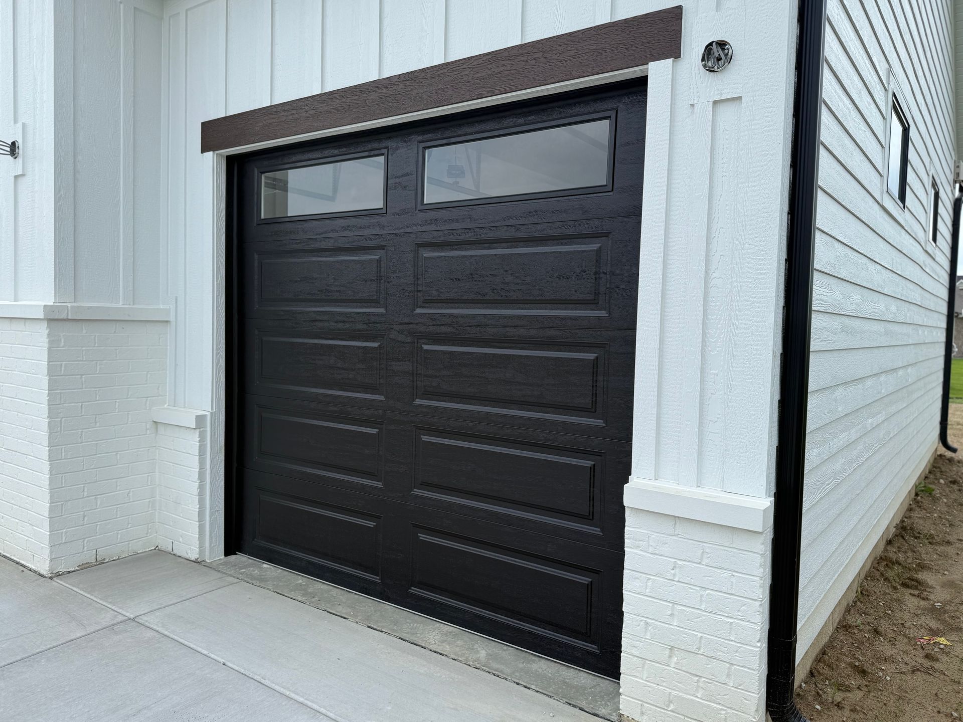 Black garage door with small windows on a white building exterior