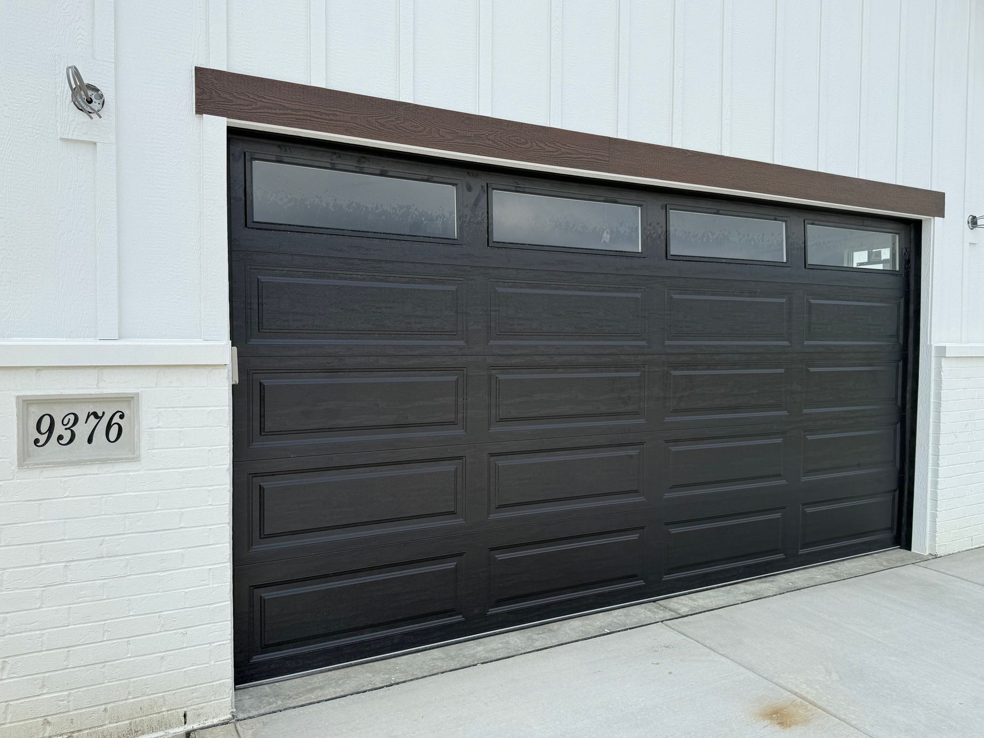 Dark brown garage door on a white house exterior with address plaque 9376.