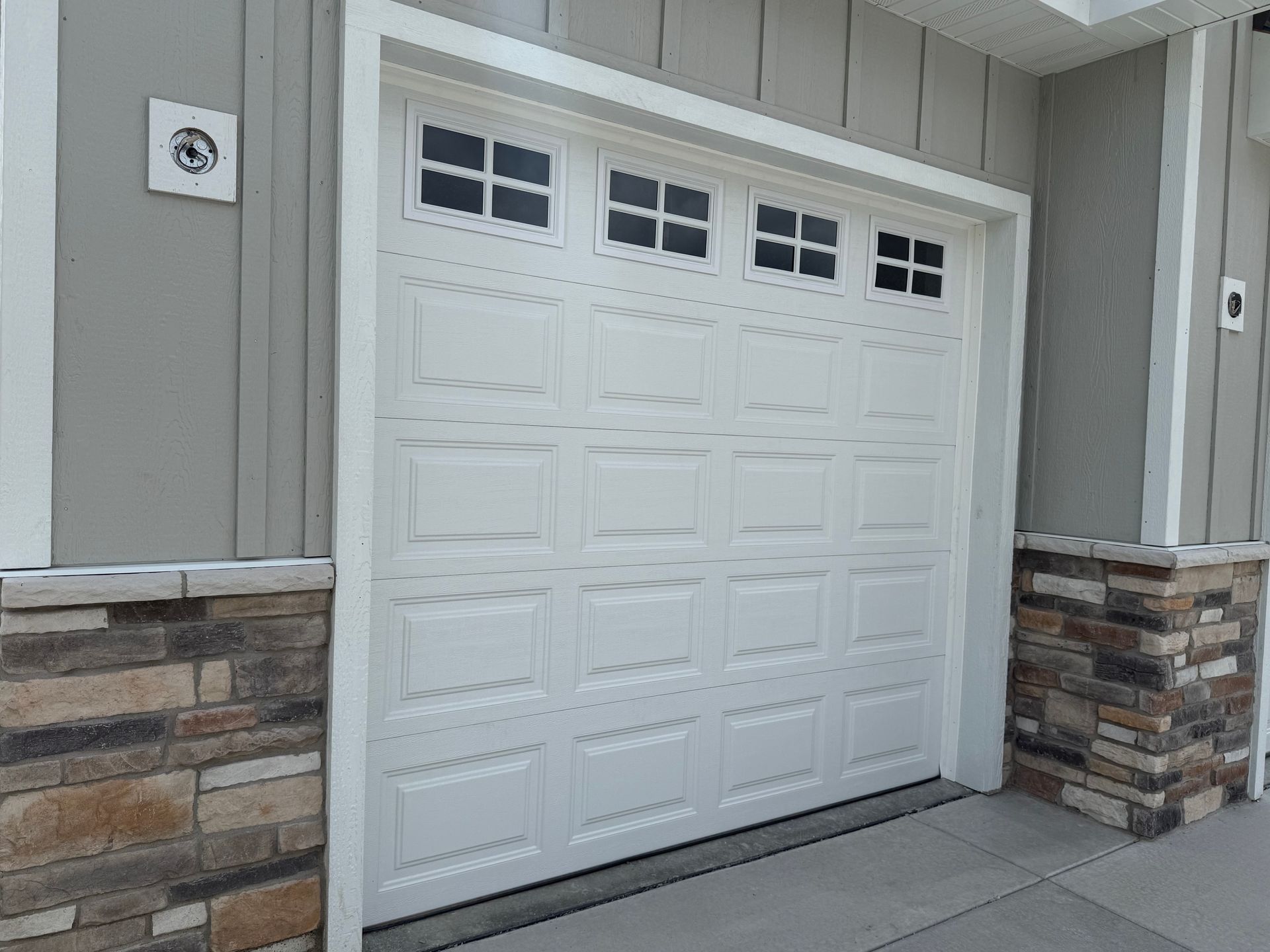 White garage door with small windows on a beige building, framed by stone trim.