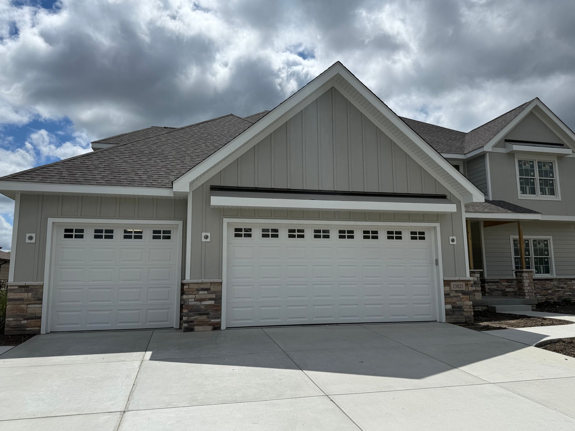 Suburban house with two garage doors and stone trim under a cloudy sky