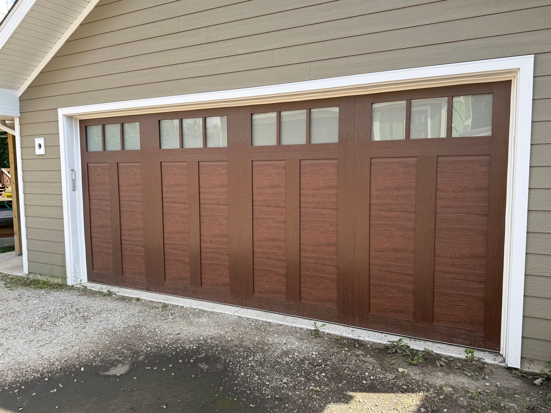 Brown garage door with small windows in a white-trimmed beige house exterior