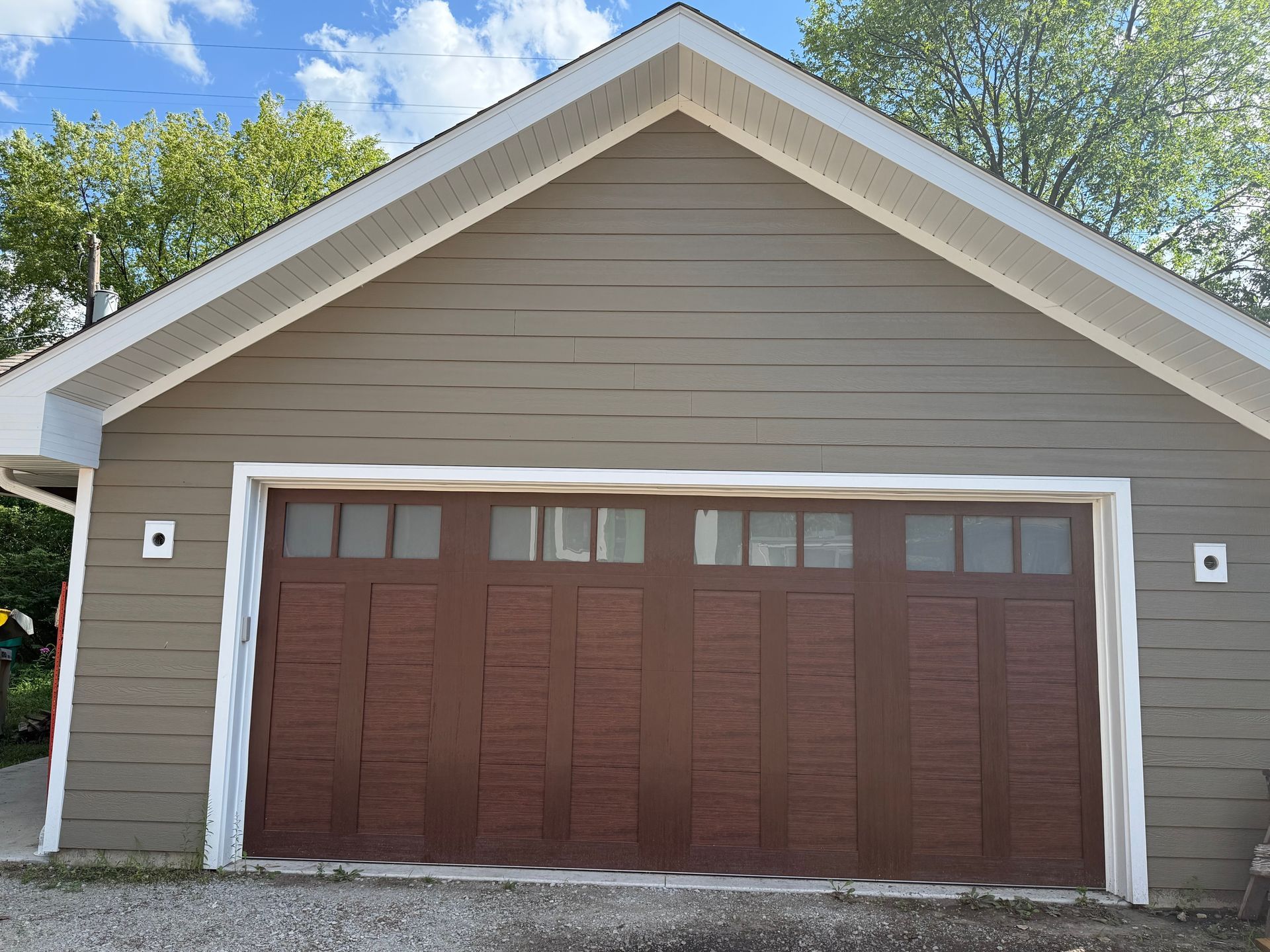 Single-car garage with beige siding, brown double doors, and white trim under a gabled roof