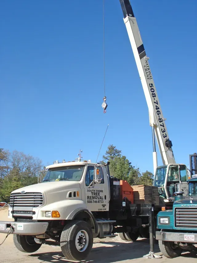 White crane truck with extended arm, hook lowered.  Blue sky background. Another truck partially visible.