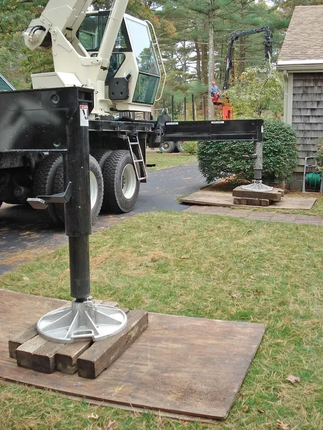 A crane with a stabilizing leg extended on a wooden platform in a yard.