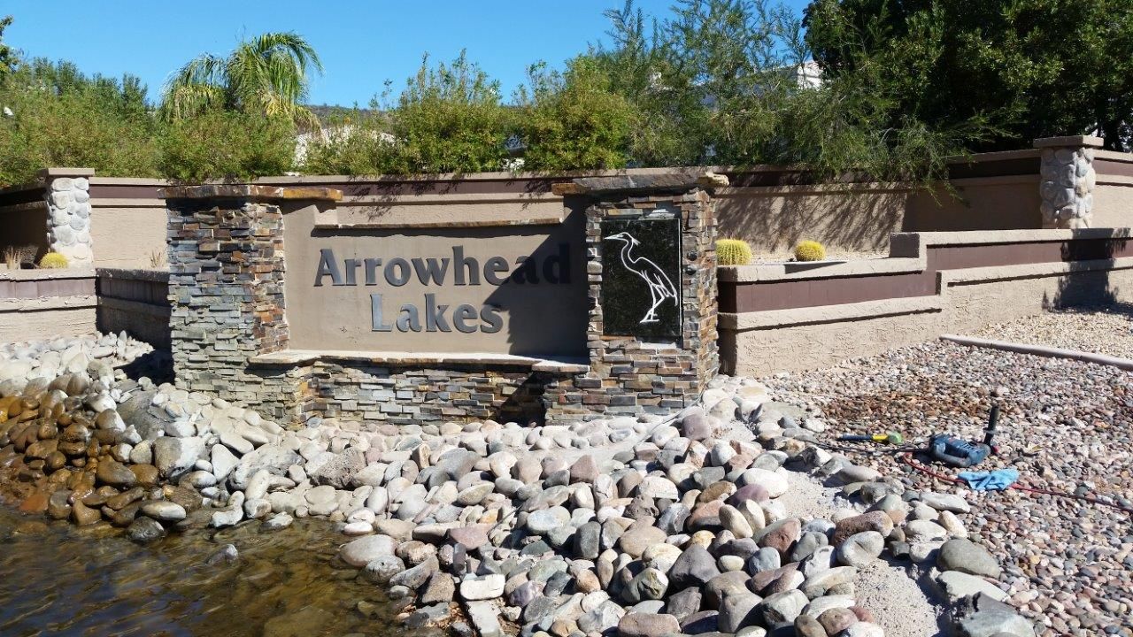 A sign for arrowhead lakes is surrounded by rocks and water