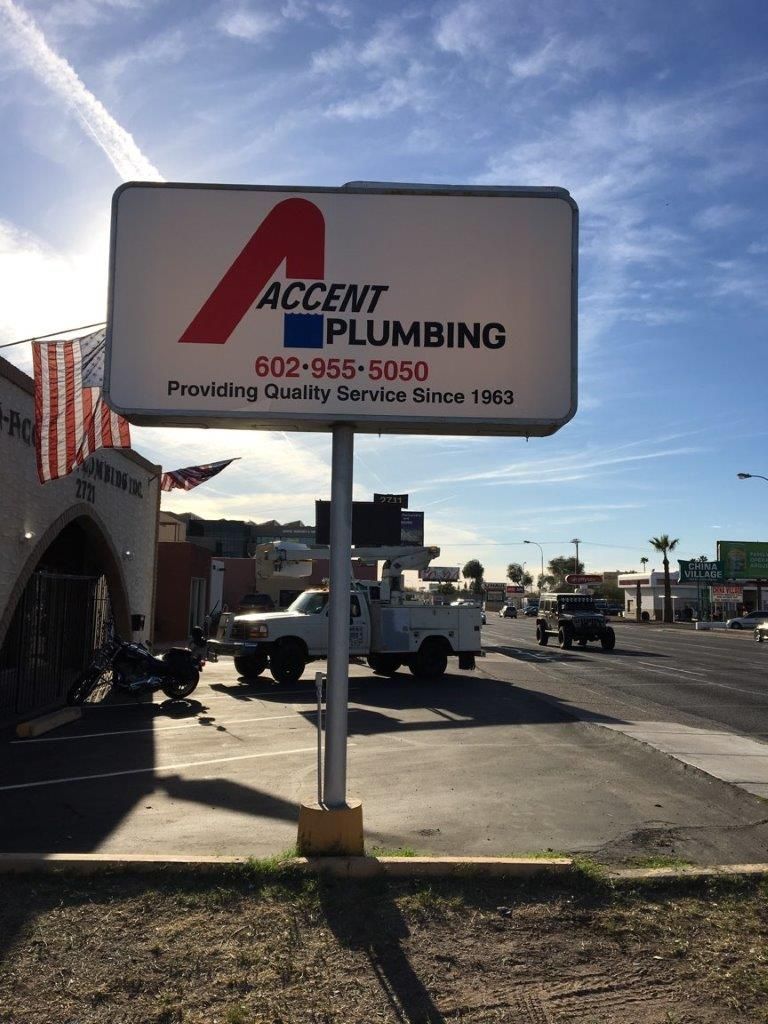 A white truck is parked in front of a sign for accent plumbing.