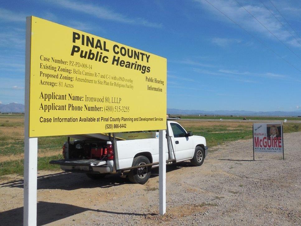 A white truck is parked in front of a yellow sign for pinal county public hearings