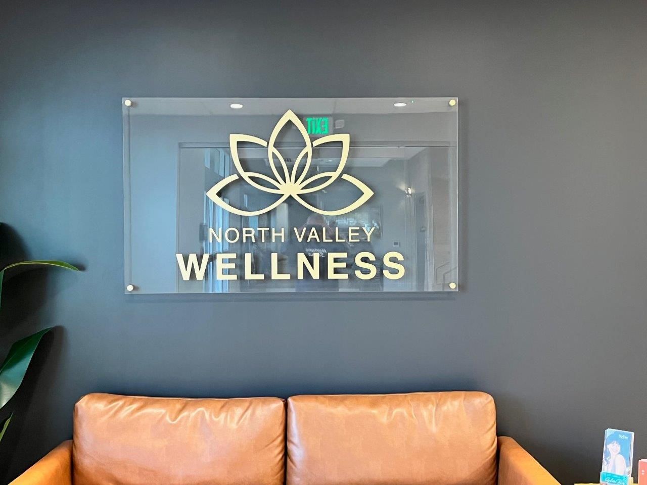 A sign for north valley wellness is hanging on a wall above a couch.