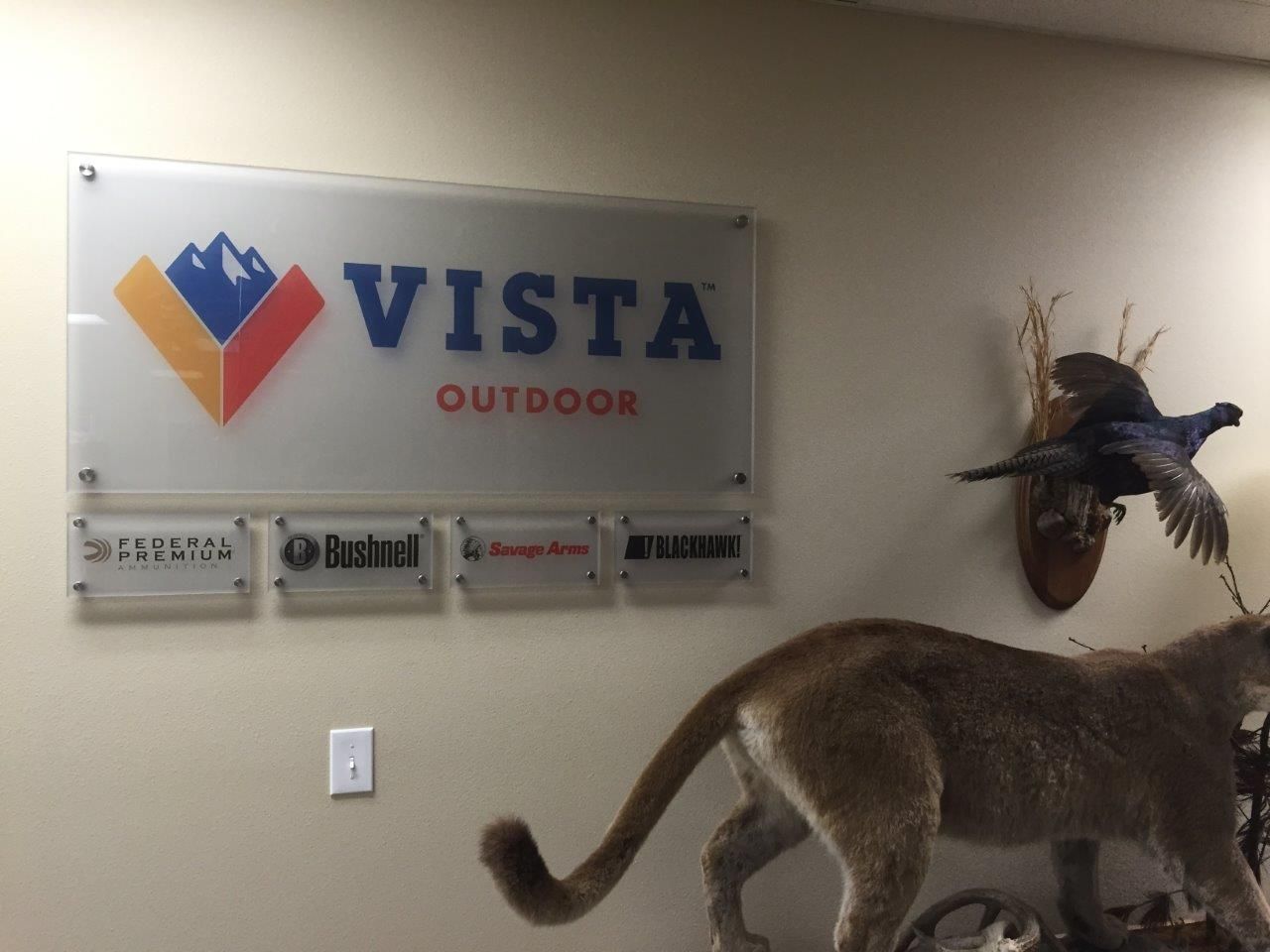 A sign for vista outdoors hangs on a wall next to a stuffed animal
