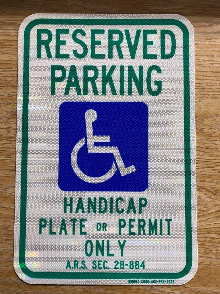 A reserved parking handicap plate or permit only sign is sitting on a wooden table.