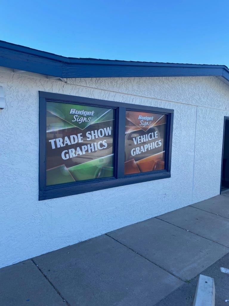 A white building with two windows advertising trade show graphics and vehicle graphics.
