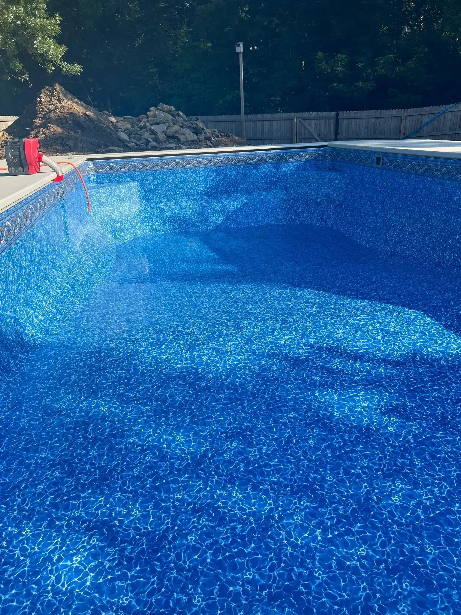 Blue swimming pool with shimmering surface; pile of dirt in background.