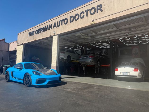 Blue sports car and white sedan outside The German Auto Doctor garage on a sunny day