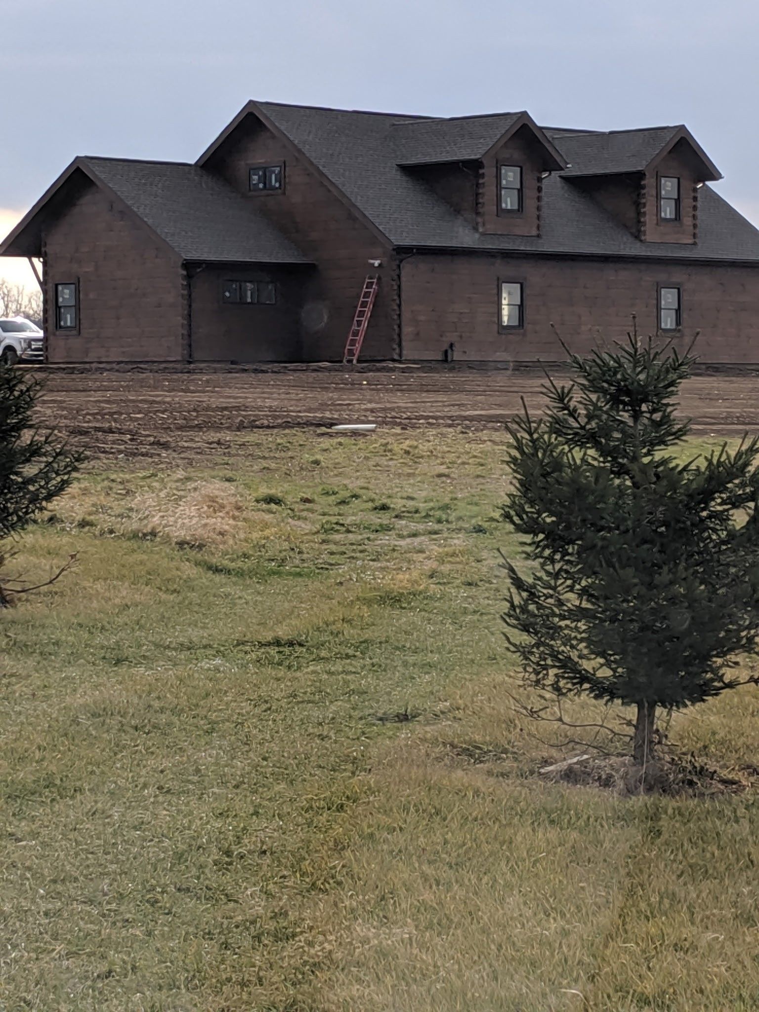 Brick house with dark roof on a grassy lot, bordered by a low retaining wall and small trees.