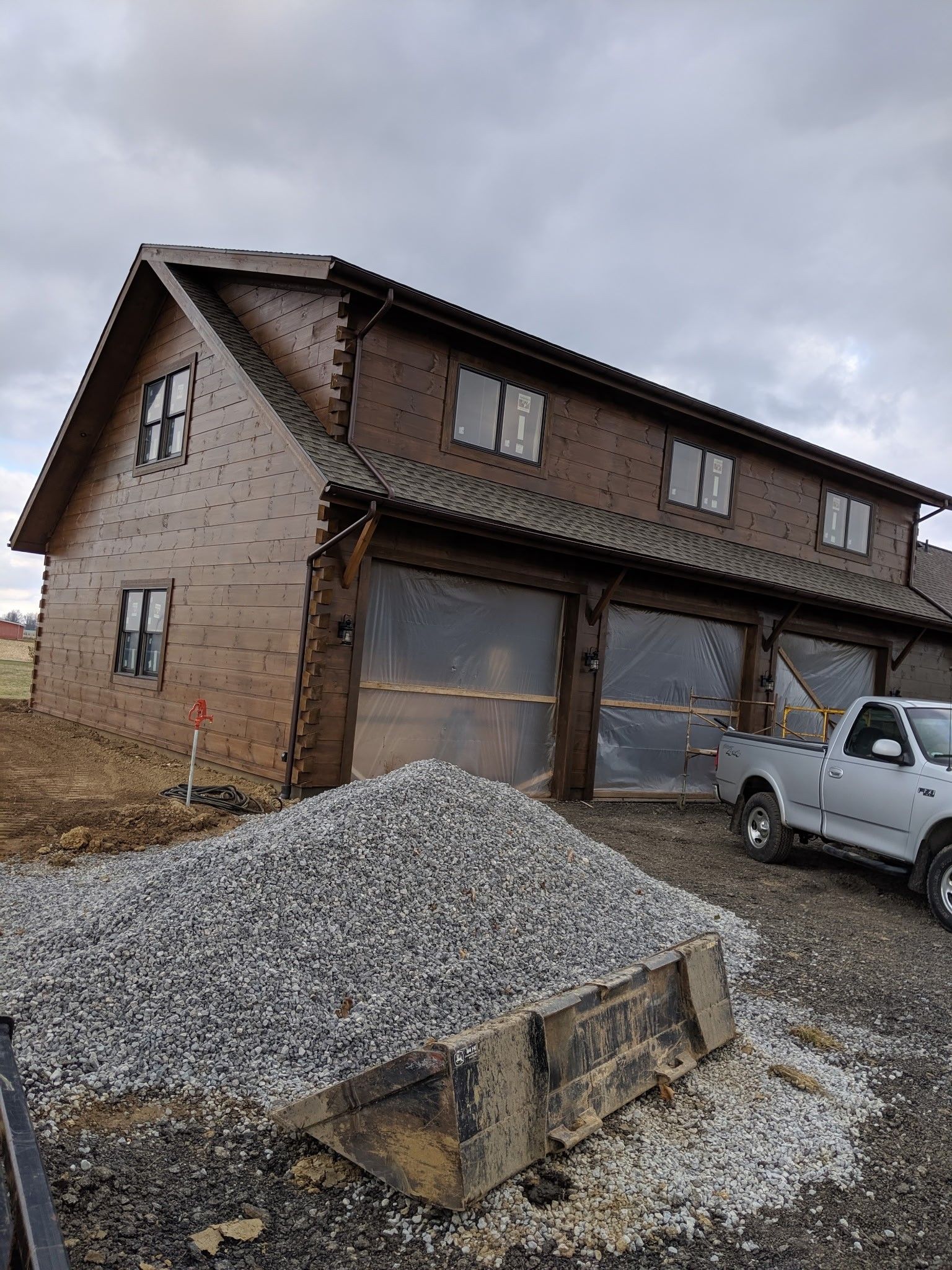New brick house with two garage doors, gravel pile in front, and a white pickup truck under a cloudy sky