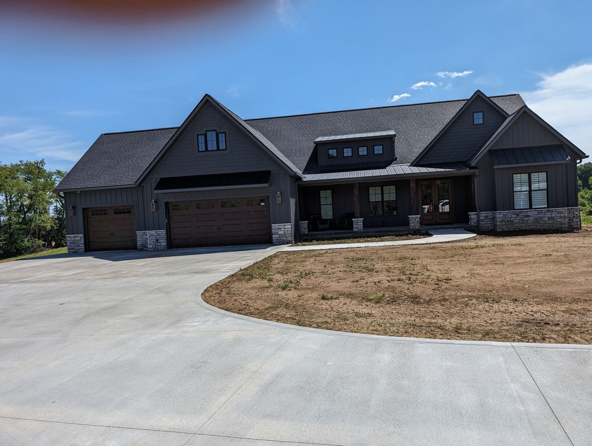 Large dark-gray suburban house with a three-car garage and wide driveway under a blue sky