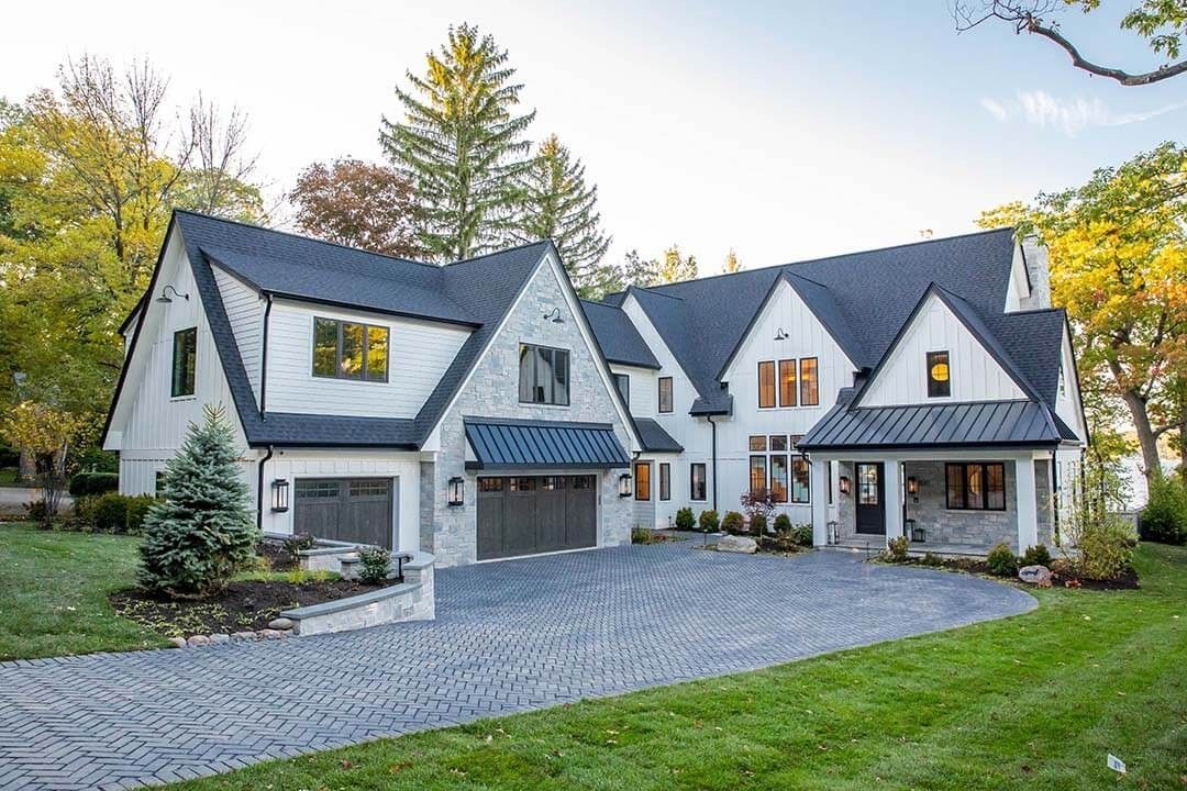 Large white house with dark roof, stone driveway, and trees in the yard