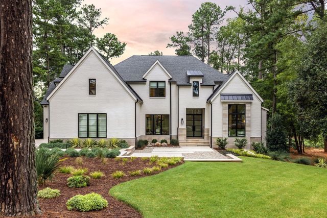 White modern house with black roof, stone entry, and landscaped front yard at dusk