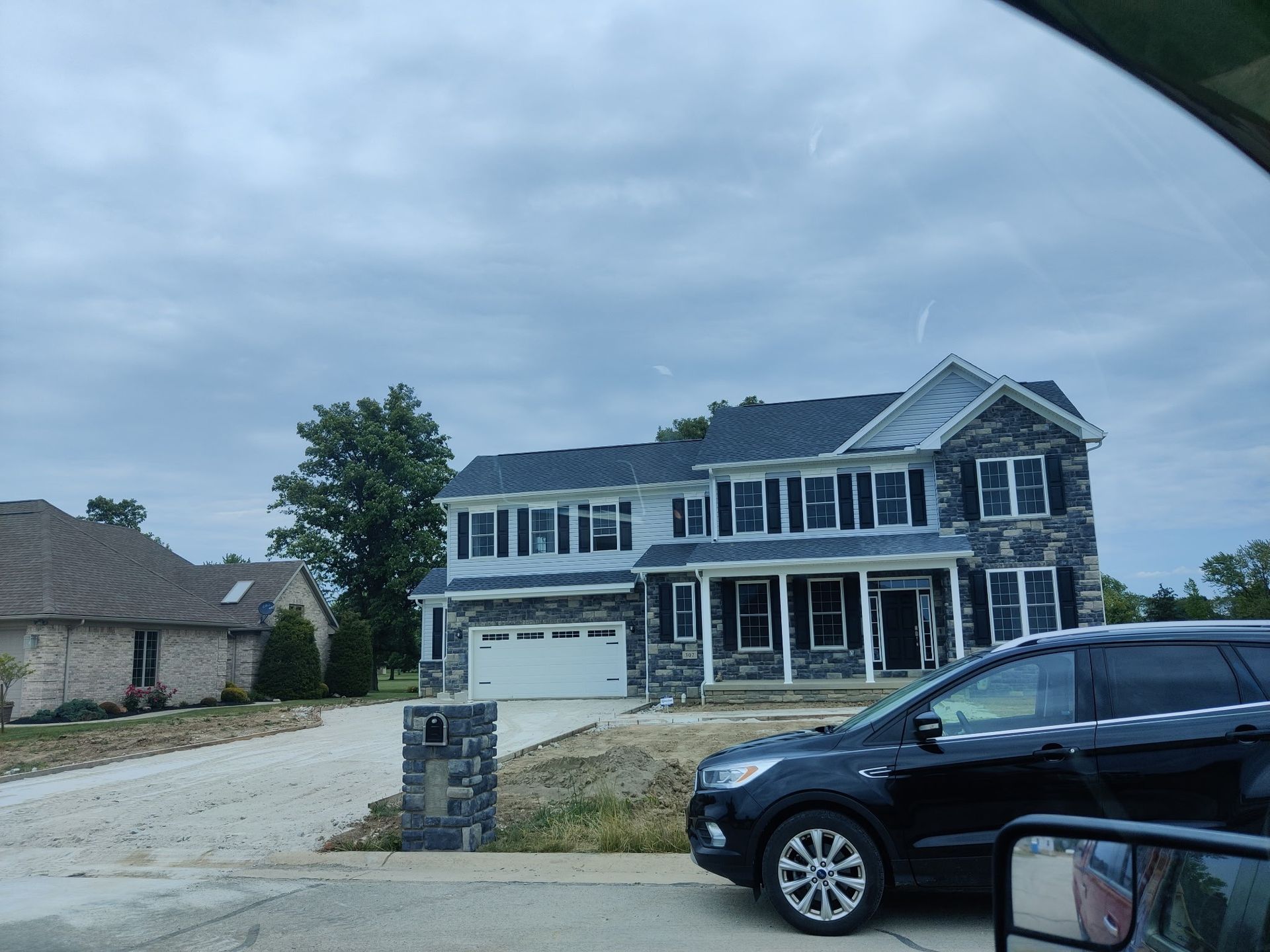 Two-story gray house with black trim and a parked black SUV in a suburban driveway under cloudy skies