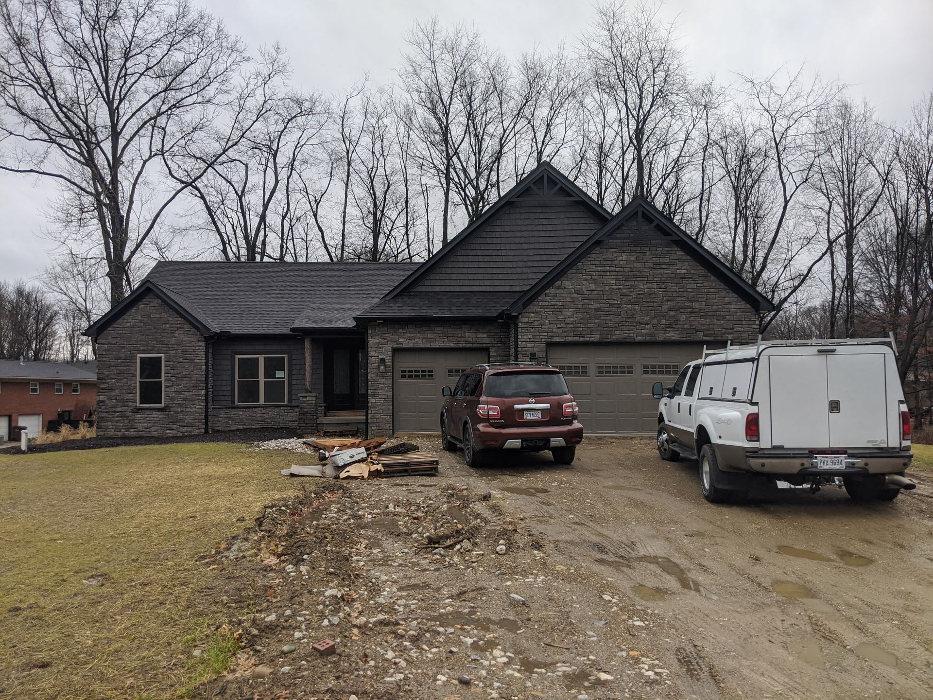 Front view of a dark house with a gravel driveway, a red SUV, and a white work van.