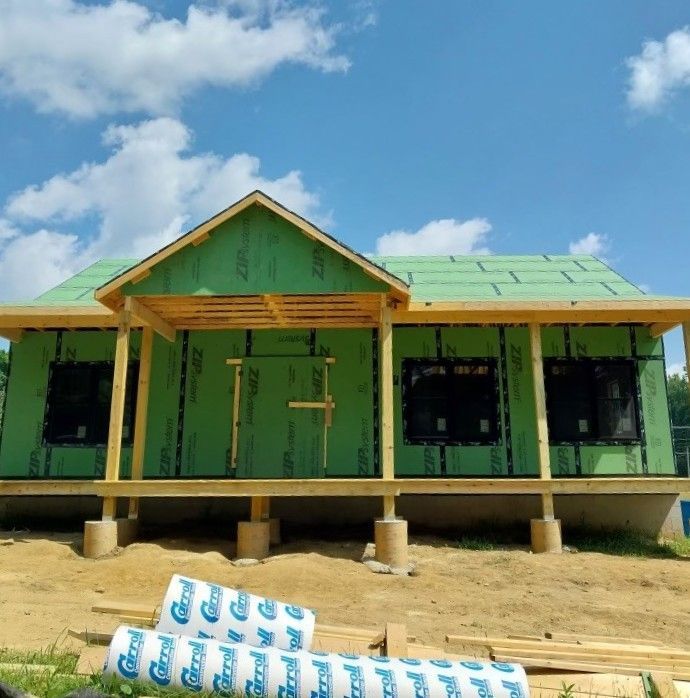 Green house under construction with unfinished porch and roof, stacks of building materials in front