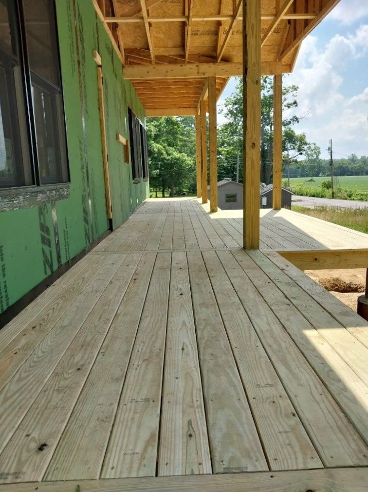 Wooden porch with green exterior walls and posts overlooking a grassy landscape