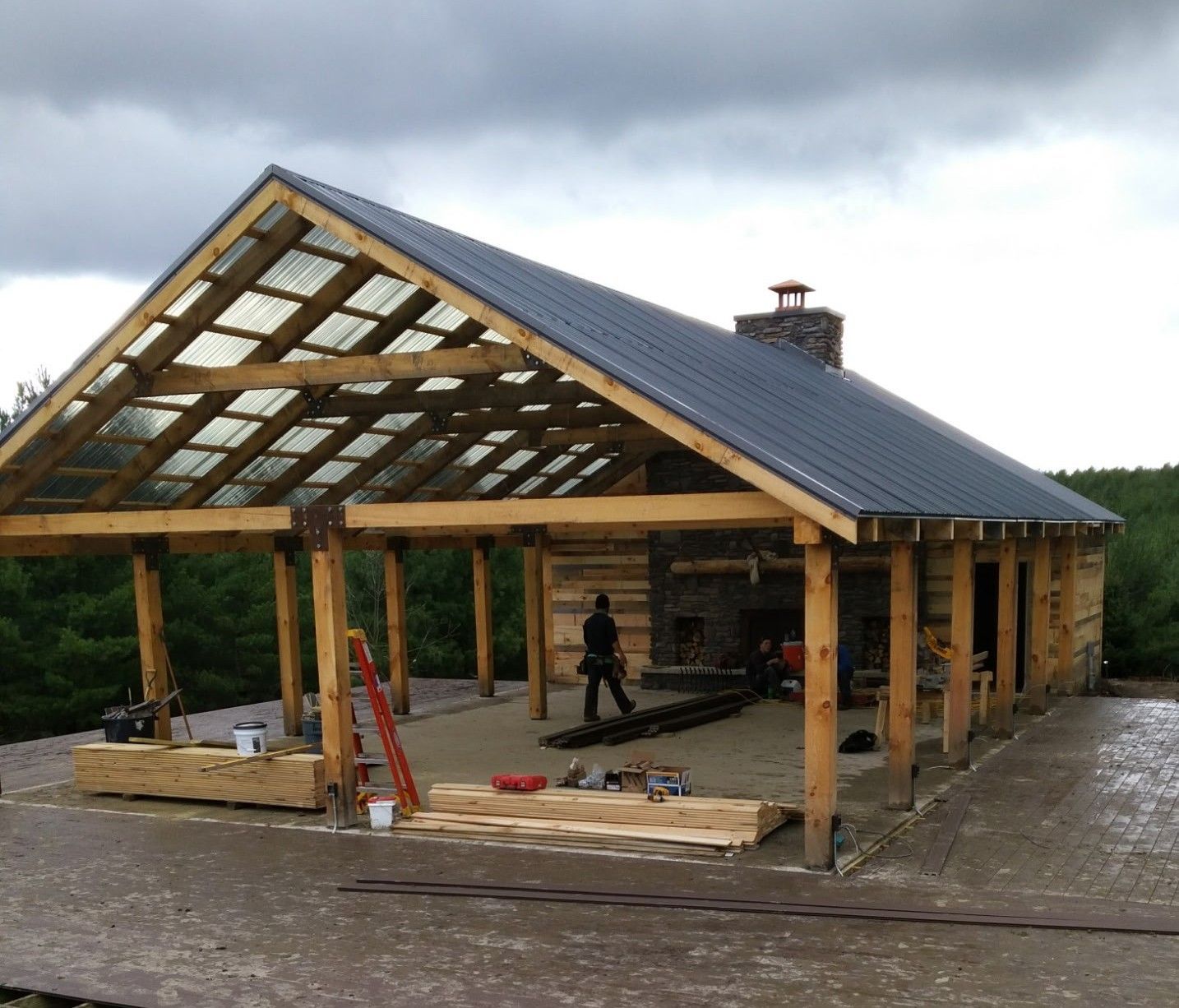 Partially built wooden pavilion with a dark roof on a muddy construction site