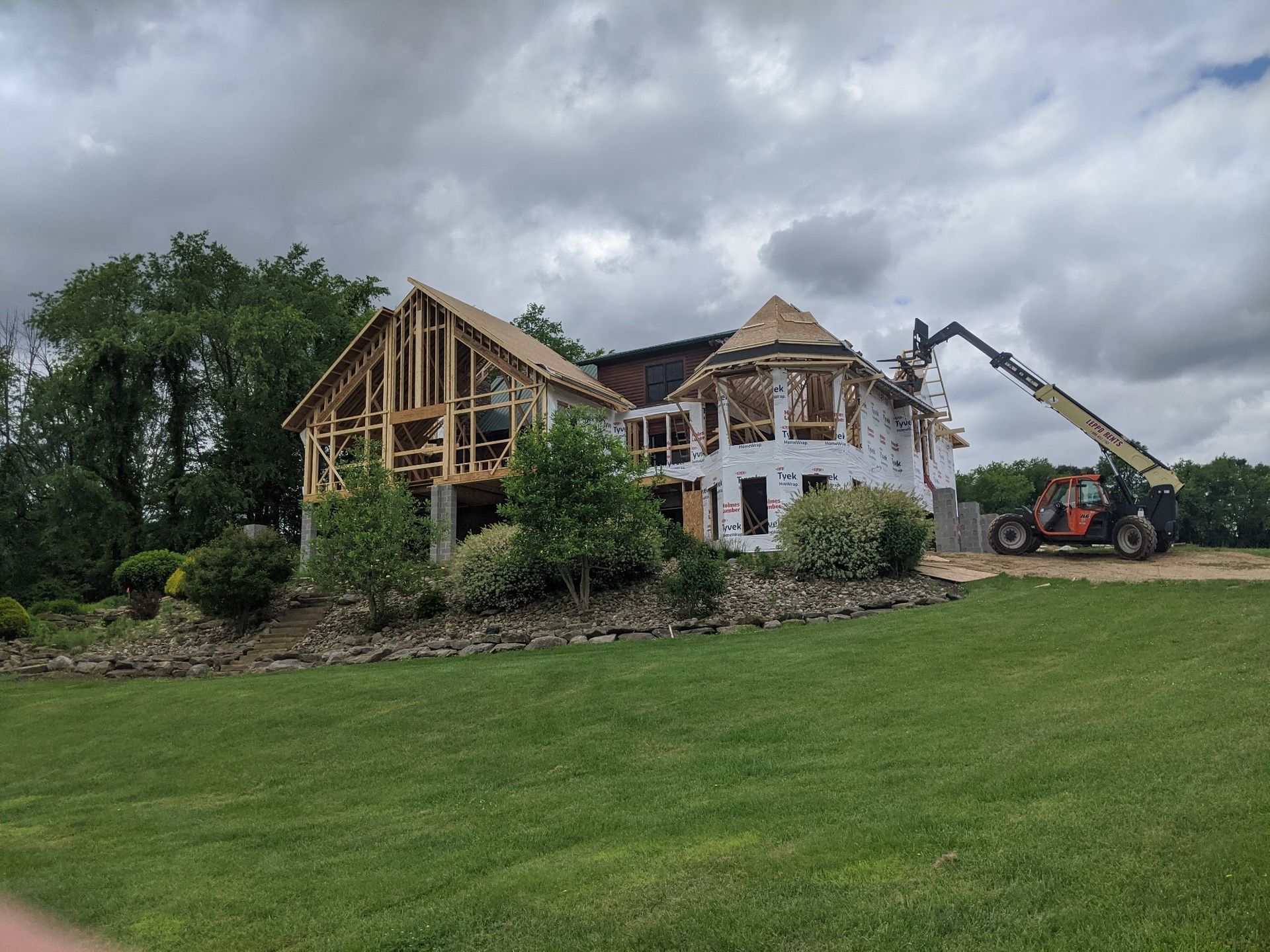 Partially demolished house under renovation with a crane and excavator beside a grassy yard