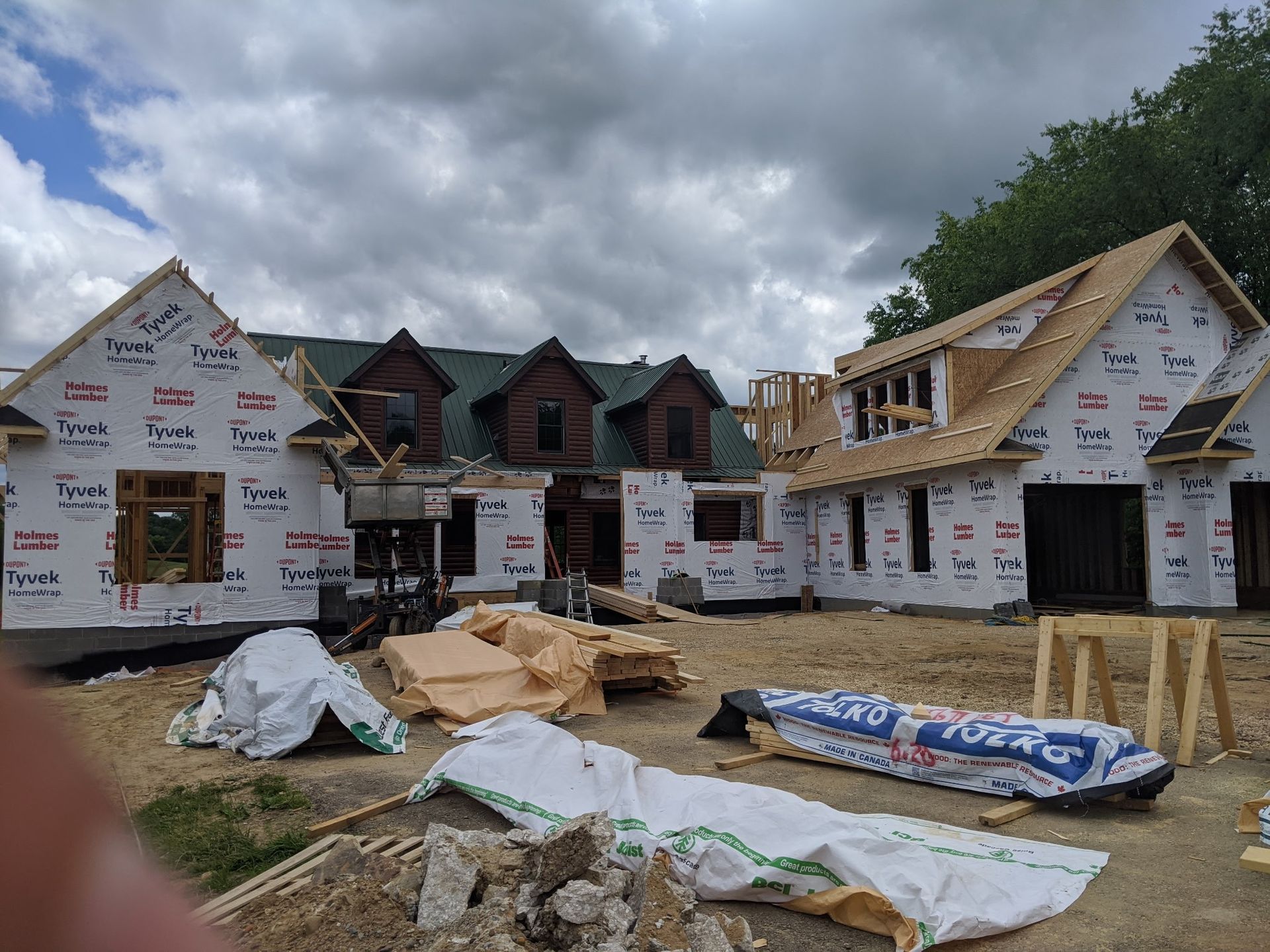 Partially built houses wrapped in white housewrap under a cloudy sky, with construction materials in the foreground