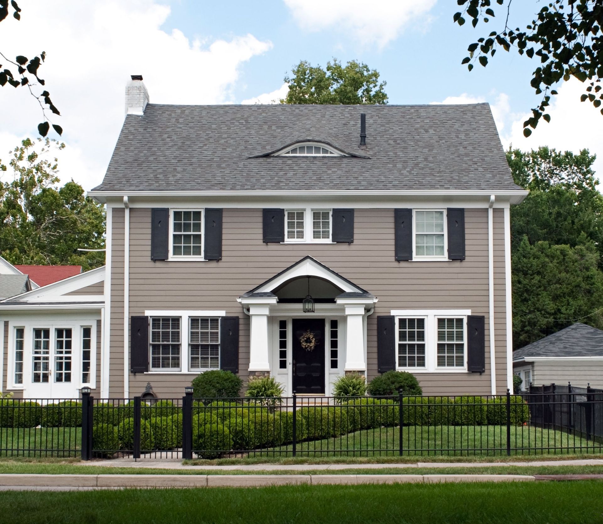Two-story gray house with white trim and black shutters behind a black iron fence