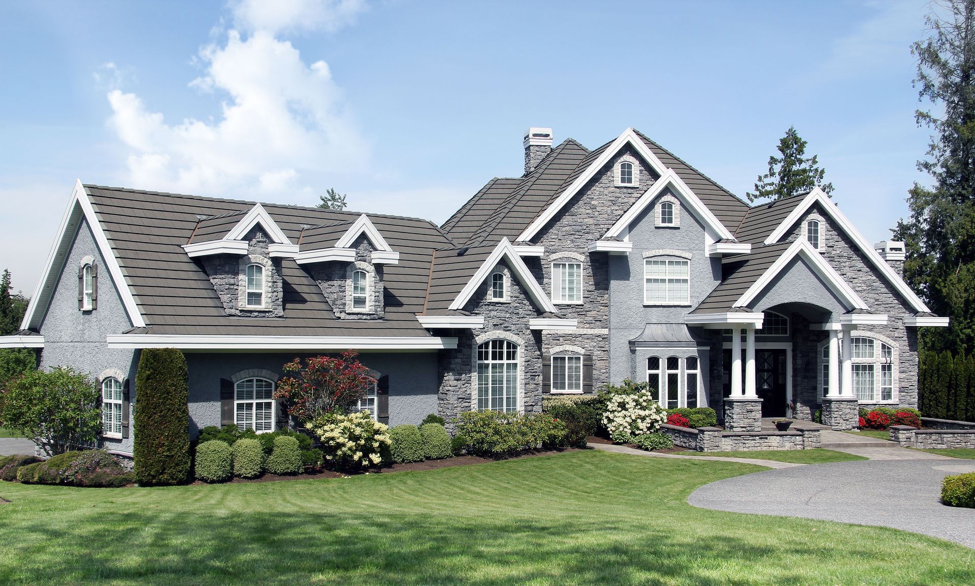 Large gray stone house with gabled roofs, white trim, and a manicured lawn