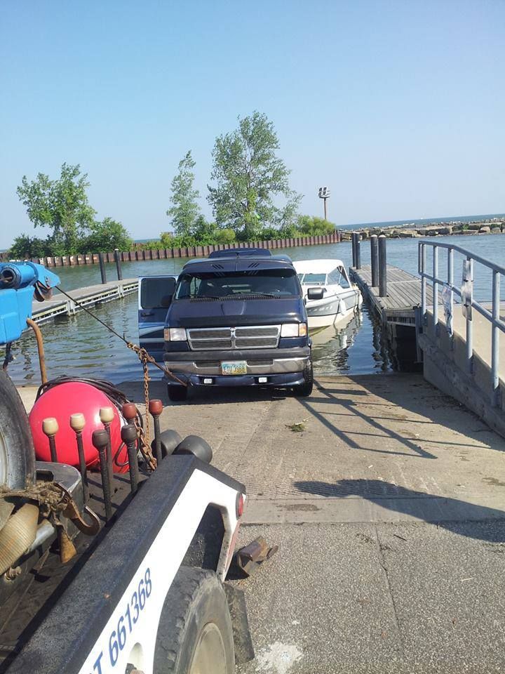 Dark blue van pulling a boat onto a dock at a lake.