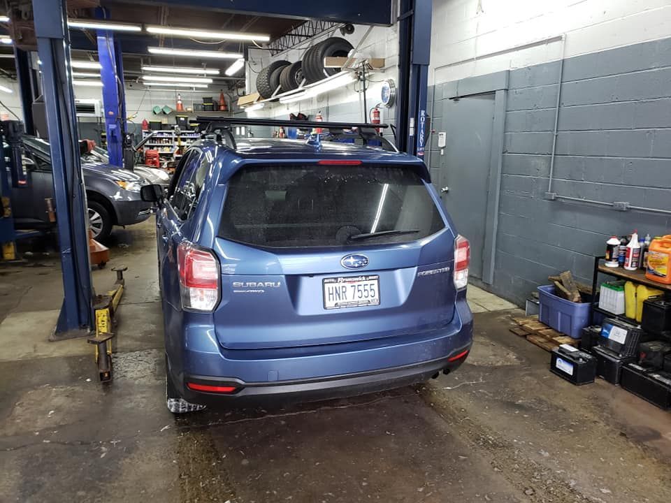 Blue Subaru Forester in a garage with a car lift, tools, and tires.