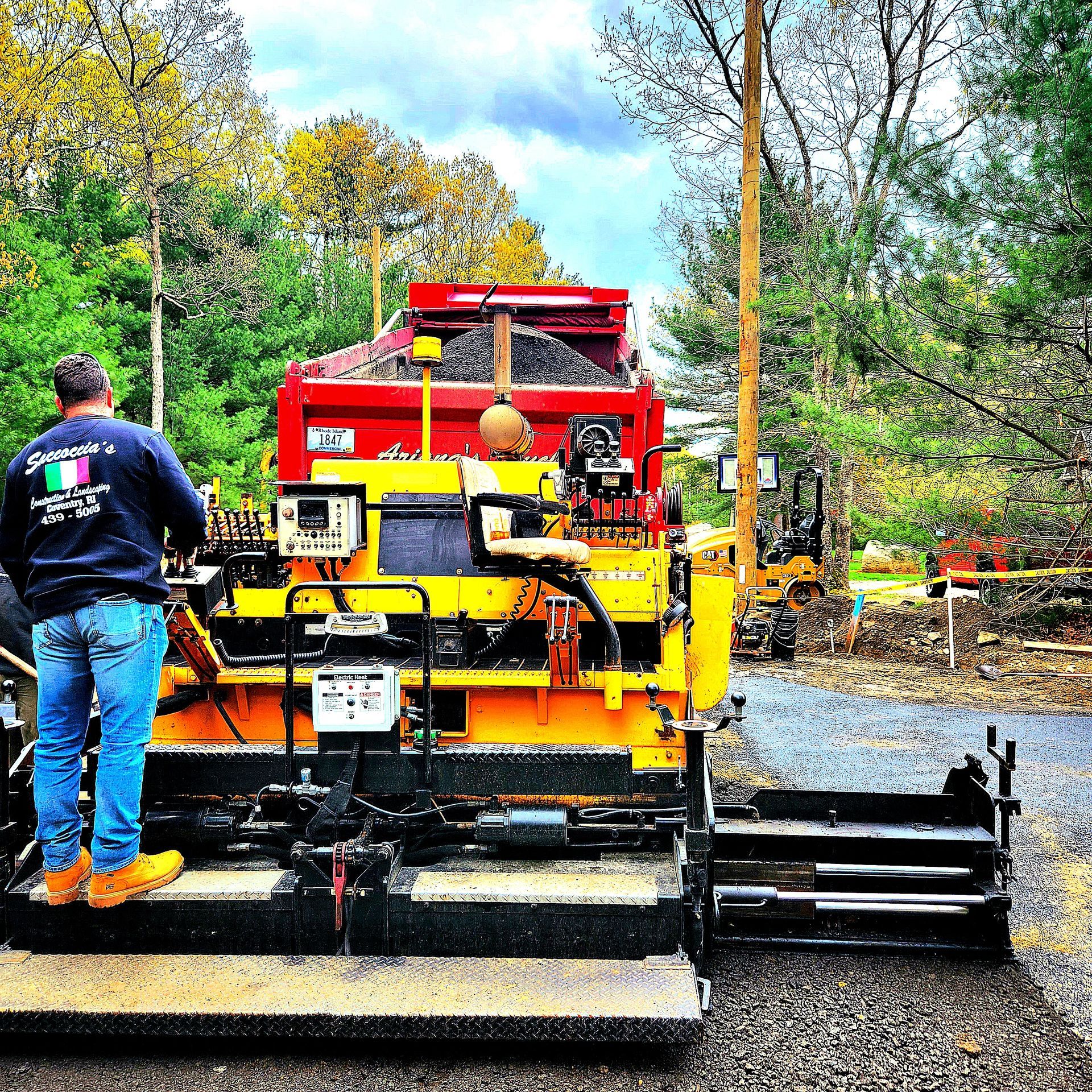 A man is standing in front of a yellow and red truck that says  'asphalt' on it