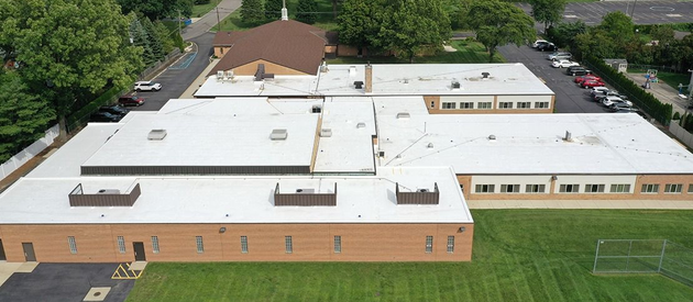 Aerial view of a large brick-and-white school building with a green lawn and trees surrounding it.