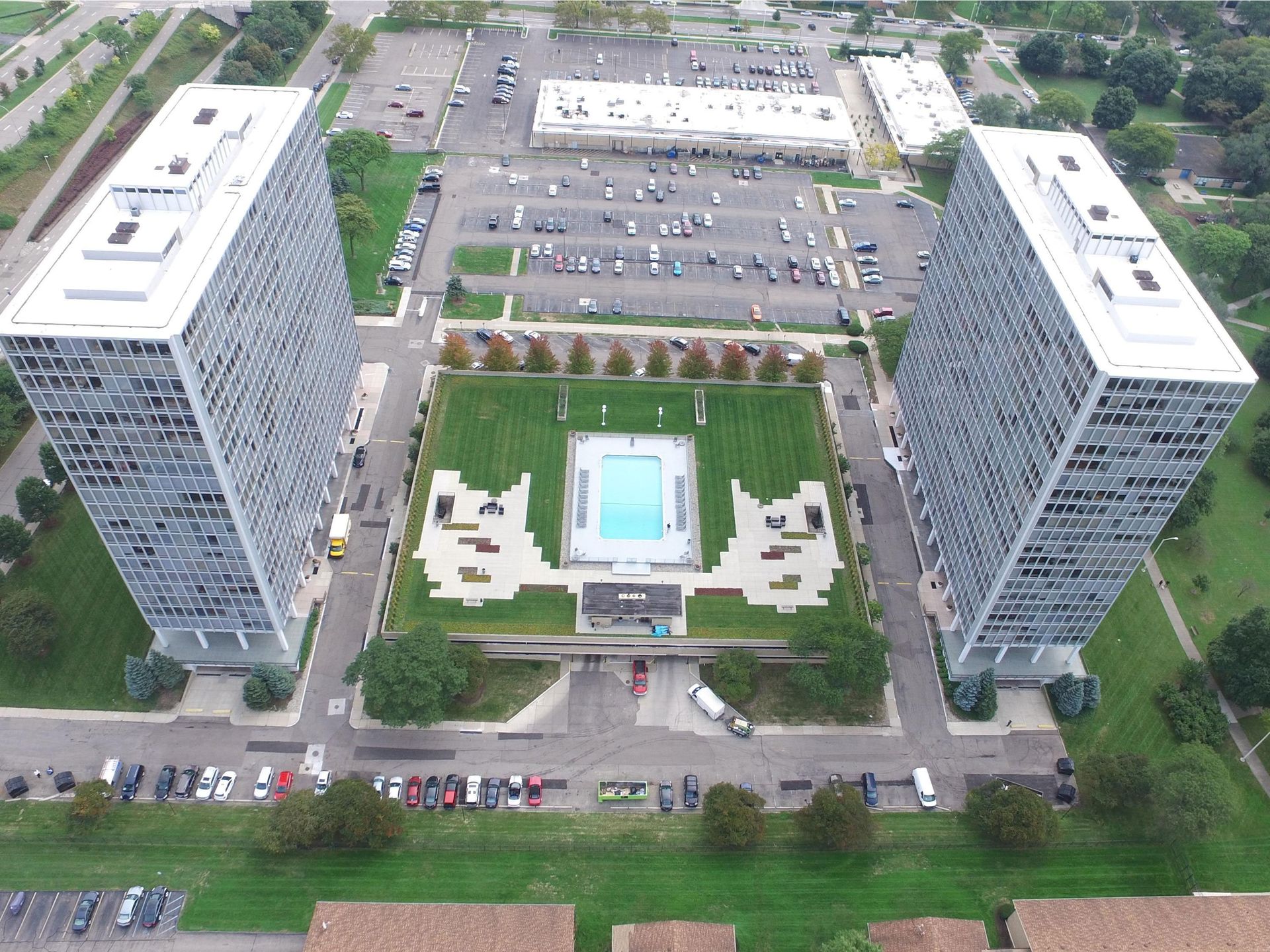 Aerial view of two high-rise apartment towers flanking a central courtyard with a pool and parking lot
