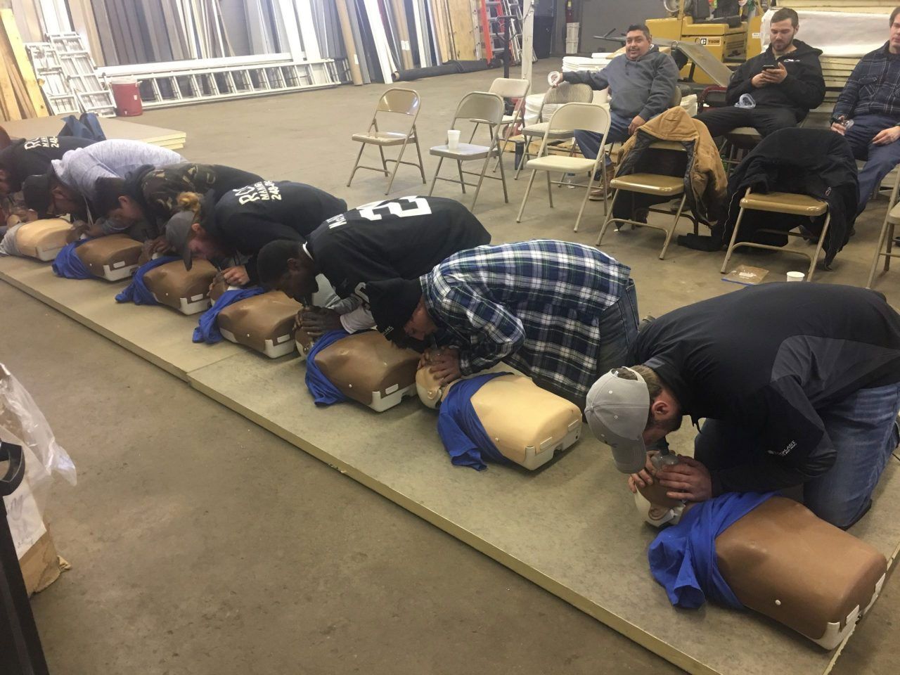 People on padded blocks kneel in a line on a carpeted floor during a group exercise in a classroom.