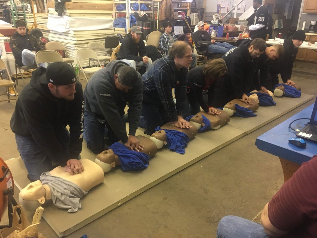 People practicing CPR on mannequins in a training room, with instructors overseeing them.