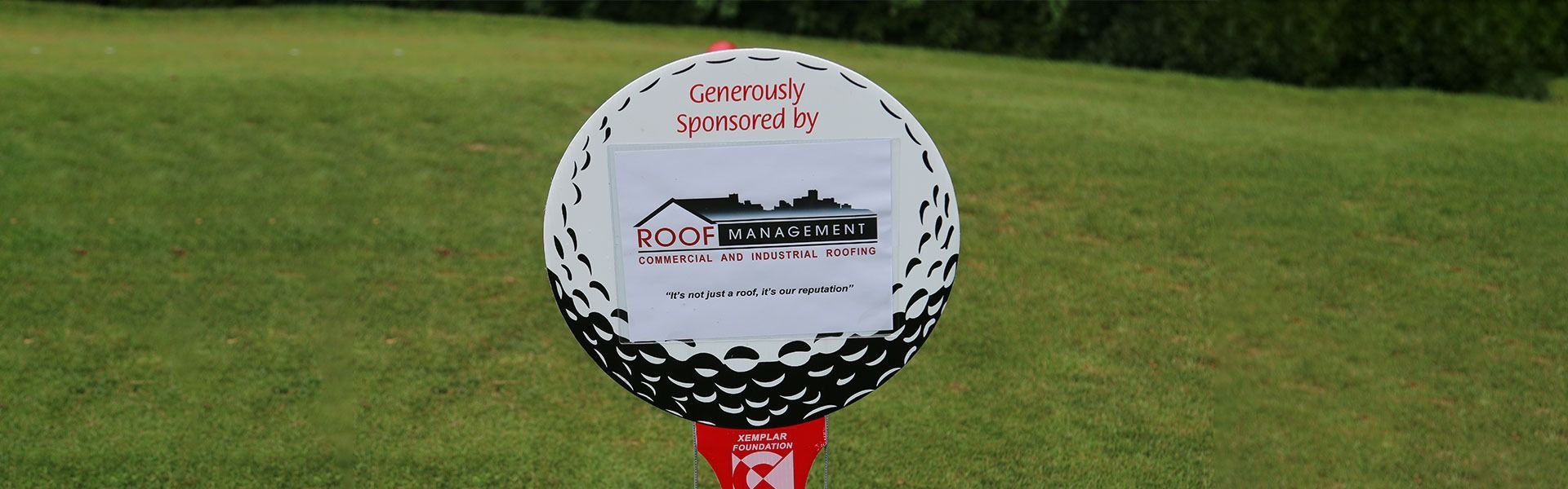 Golf tournament sign on a tee marker on a green course, with a white and black patterned ball-like top.