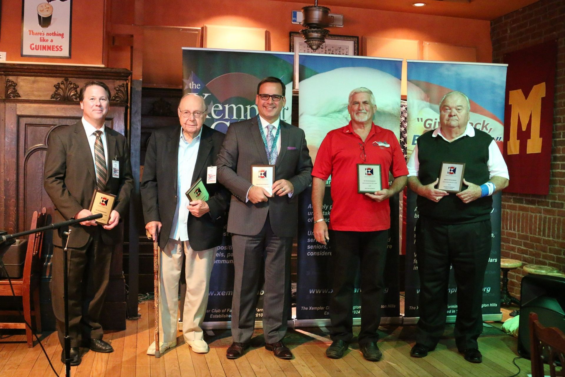Five men on a stage holding awards during a formal ceremony, with a colorful backdrop behind them