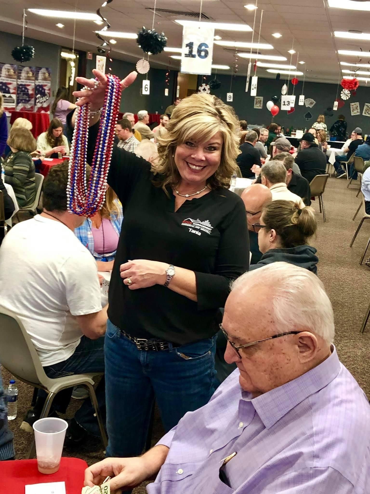 Woman smiling in a crowded banquet hall, standing beside seated guests at a table.