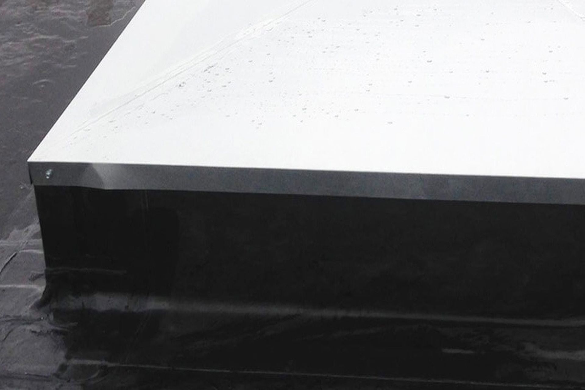 White metal table or platform with a dark base, viewed at an angle on a stone floor