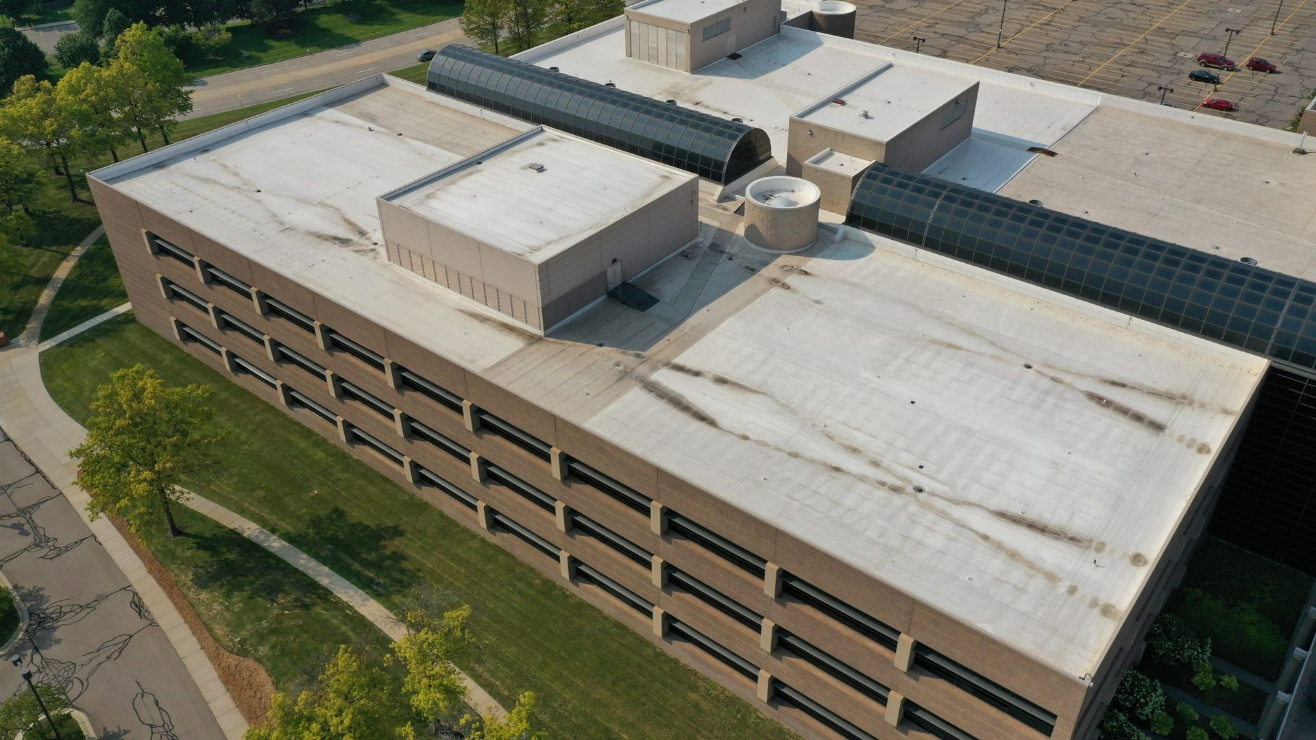Aerial view of a large tan office building with a white rooftop and surrounding trees and roads