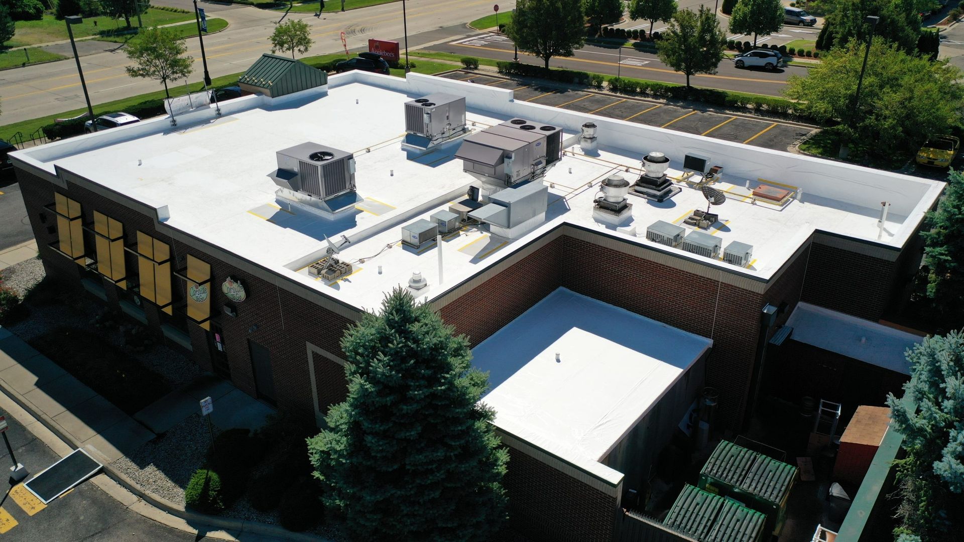 Aerial view of a flat-roof commercial building with HVAC units and nearby trees