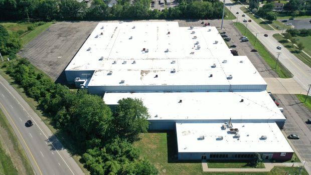 Aerial view of a large white-roofed industrial building beside a road and trees.